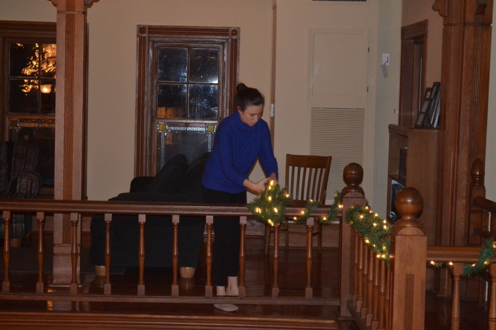 Senior Brittani Edge wraps a lighted garland around the balcony railing of the CCM. “This is my third year helping with Hanging of the Green,” Edge said. Photo Courtesy of Shelby Sparks